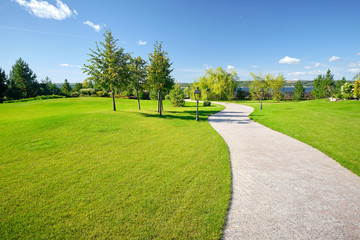 sunny morning on a green golf course with winding path, lanterns and trees with a lake in the background - 264517488
