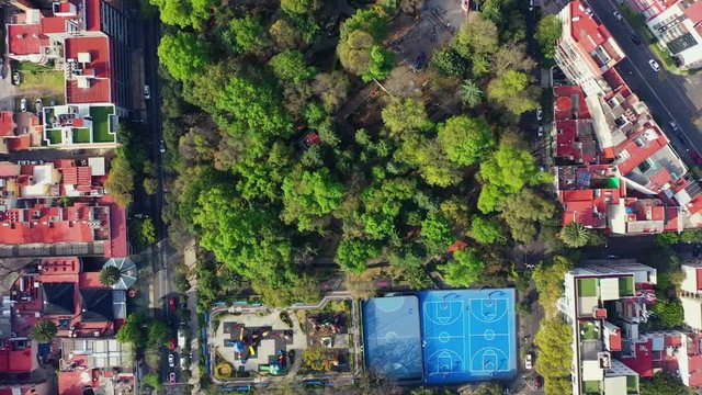 DRONE FLIGHT OVER PARK IN MEXICO CITY RESIDENTIAL AREA. KIDS PLAYGROUND COLORFUL, BLUE BASKETBALL COURT, AND CITY STABLISH