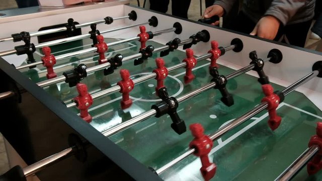 People Play Table Soccer. Red and black pieces of foosball players spin and hit the ball. Hands twist levers to hit the ball. Table soccer player kicking the football at goal