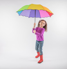 Little girl in red rain boots with colorful rainbow umbrella