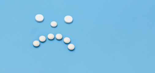 Banner. Sad face of white round pills on blue background. Place under the advertising inscription