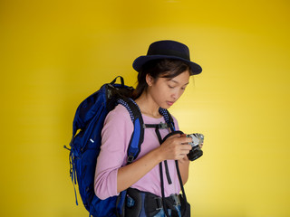 Searching for inspiring places. smiling adventure tourist woman with backpack and film camera taking photo isolated on yellow