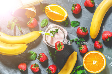 banana, strawberry and orange smoothies with mint in a glass with a straw on the table, top view