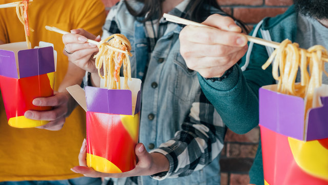 Millennials eating habit. Takeout food. Unhealthy nutrition. Hands with Chinese noodles boxes closeup. Cropped shot. - Powered by Adobe