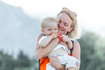 Young mother holding her little son in her arms and they are played against the backdrop of a mountain landscape