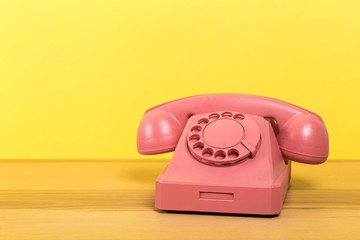 Vintage pink telephone on wooden table with color wall background