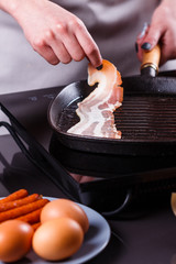 young woman in a gray apron fries bacon