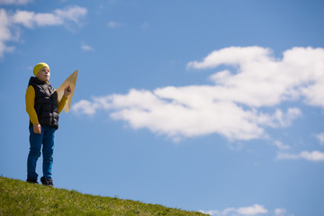 Portrait of a boy standing on top of a hill and about to launch a paper airplane into the sky. Happy child with airplane in hand. Educational games in the fresh air
