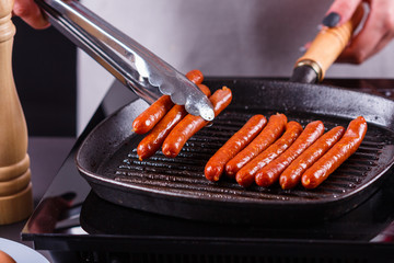 young woman in a gray apron fries sausages