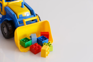 Obraz premium Bright color toy bulldozer on a white table. Multi-colored tractor collects cubes in the bucket. Early development. Kids toys