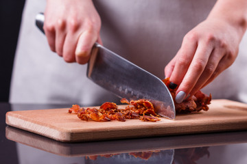 young woman in a gray apron cuts roasted bacon