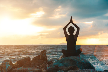 Silhouette young woman practicing yoga on the beach at sunset.