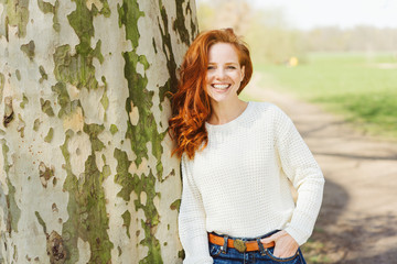 Relaxed happy young woman leaning against a tree