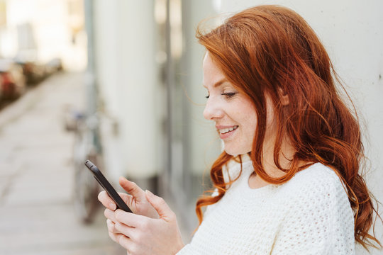 Side portrait of red-haired woman with smartphone