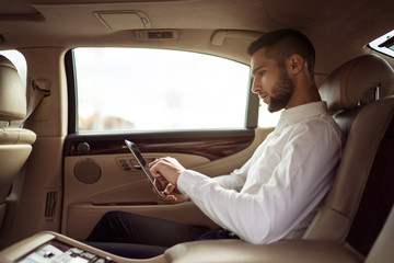 Man uses pc tablet sitting in back seat of car, businessman in taxi