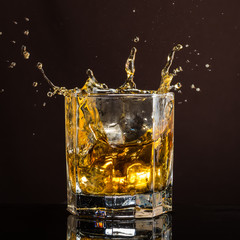 hexagonal glass of whiskey with ice and splashes from an abandoned and falling ice cube