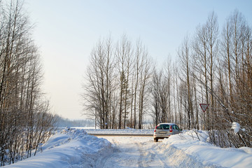 White snow road with car amoung winter trees in forest in a sunny day