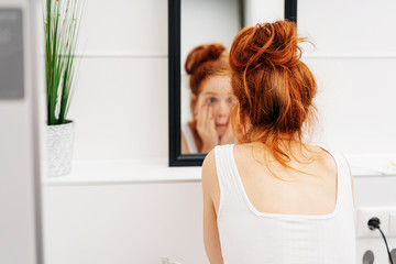 Bleary eyed woman peering at herself a the mirror