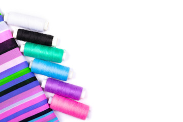 Sewing. Background of striped fabric and spools of threads of different colors on a white background. Flat Lay, space for text, Copy space, top view