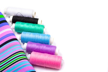 Sewing. Background of striped fabric and spools of threads of different colors on a white background. Side view, space for text, Copy space,
