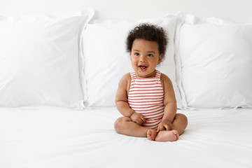 Happy black baby sitting on bed