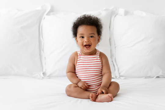 Smiling baby with afro hair sitting on bed