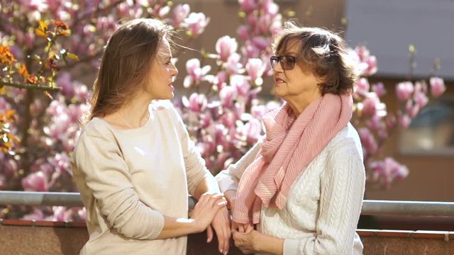 Conversation mother and daughter. Two women are standing on the balcony against each other and have fun talking. Spring day blooming magnolia tree