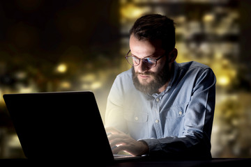 Young handsome businessman working late at night in the office with city lights in the background