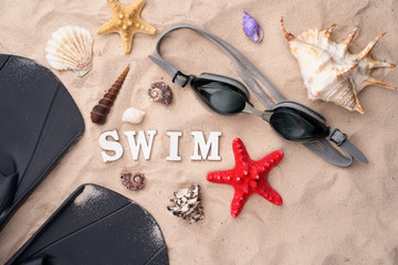Swimming goggles and flippers on the sand with shells and starfishes. © nuclear_lily
