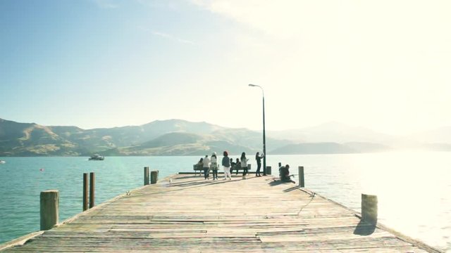 People are walking down pier in summer, bright blue water in popular tourist town Akaroa, Christchurch, New Zealand, Sun is shining in summertime