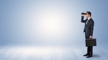 Businessman looking forward with binoculars in an empty space
