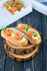 Tasty and beautiful eclairs on a wooden board. Appetizing dessert with red fish, cucumber, cheese and greens.