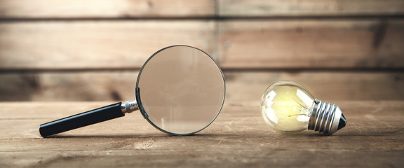 Magnifying glass with light bulb on a wooden background. Concept of creativity, idea, business