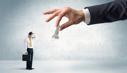 Little businessman is afraid to make the next step in his chess game with graphs, charts and...