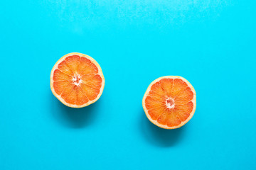 Two red orange grapefruit slices on blue background, flat lay, minimalism, summer creative concept