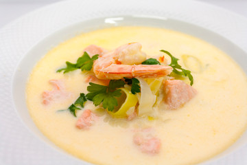 big king prawn with a pile of salmon in a cream soup of shrimp with parsley and lemon cooked for gourmets in a white plate on a white background in the restaurant