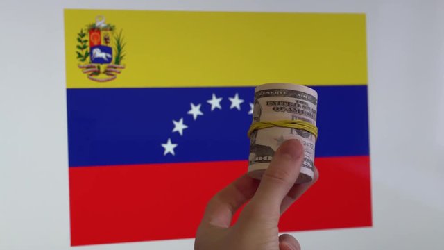 Roll of cash money  in hand, flag of Venezuela visible on the background.