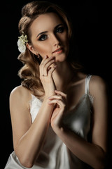 Close-up portrait of girl with blond hair and hands near the face. Bride with beautiful makeup on a dark background