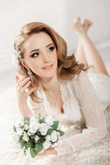 Beautiful girl with blond hair in a bright room is lying on the floor. Bride lying holding a bouquet