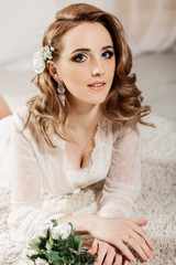 Beautiful girl with blond hair in a bright room is lying on the floor. Bride lying looking at the camera and smiling