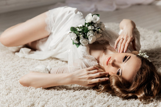 Beautiful girl with blond hair in a bright room is lying on the floor. Bride lying holding a bouquet