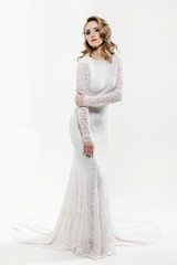 Beautiful girl with blond hair posing. The bride in a beautiful dress with a long train on a white background