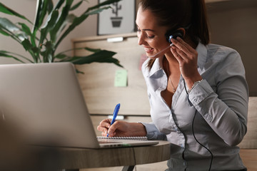 Happy customer support representative taking notes while working in call center.