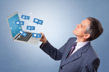 Man holding laptop with different types of social media symbols and icons

