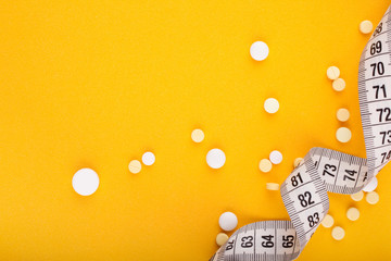 Diet vitamin pills and measure tape on yellow background