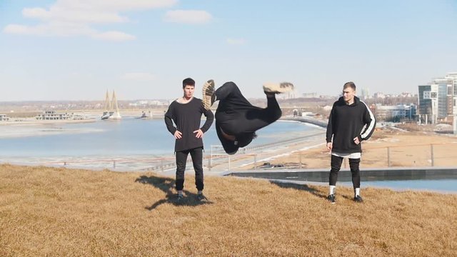 A young man and performing acrobatic tricks and flips on the grass while his friends watching him