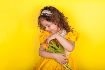 Little girl with tulips in hands on yellow background