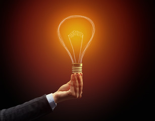 Hand holding light bulb on dark background. New idea concept