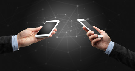 Close up of two hands holding smartphones to each other, wireless connection concept