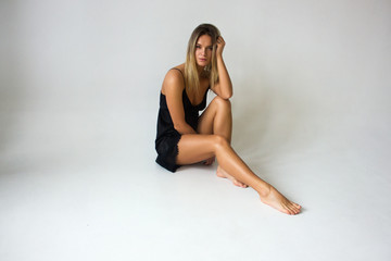 young blonde fit girl in black dress is sitting on white wall background, lifestyle concept, relax and fitness